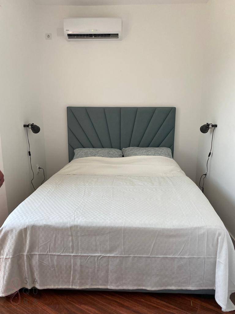 Schlafzimmer mit modernem Kopfteil, Holzboden und Klimaanlage an der Wand.
