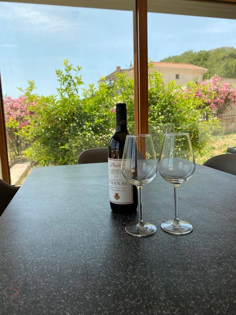 Esstisch mit Wein und Gläsern, umgeben von großen Fenstern mit Blick ins Grüne.