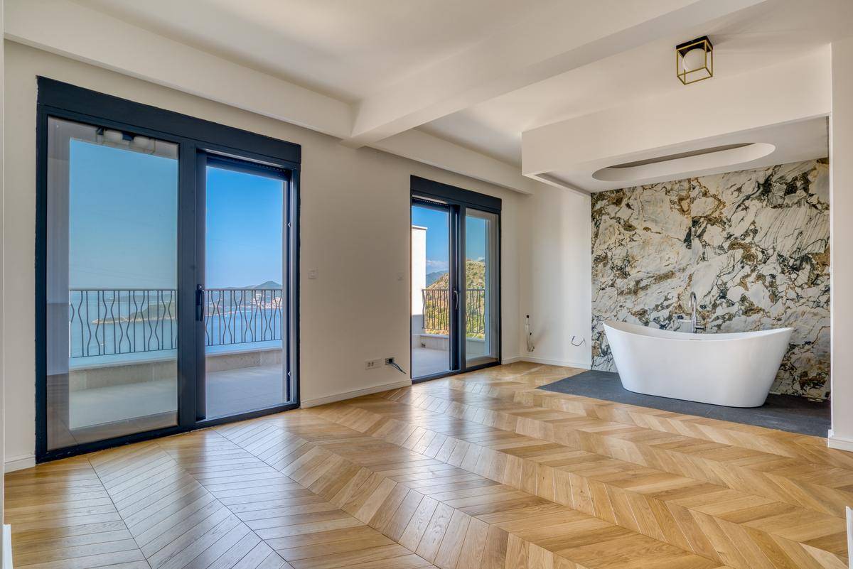 Geräumiges Schlafzimmer mit Fischgrätparkett, freistehender Badewanne und Zugang zu einem Balkon mit Meerblick.