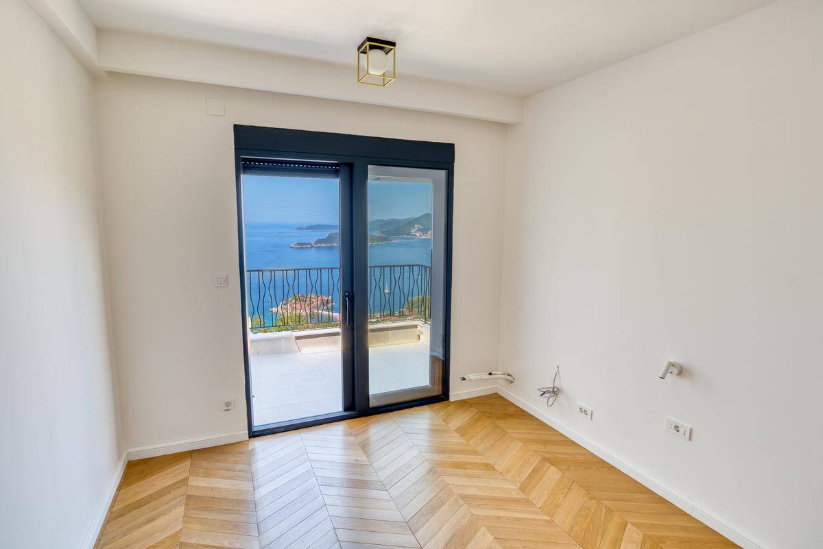Lichtdurchflutetes Zimmer mit Holzboden und Zugang zu einem Balkon mit Panoramablick auf das Meer.
