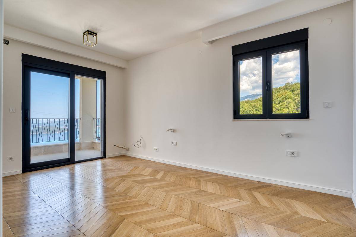 Geräumiges Zimmer mit Fischgrätparkett, Balkonzugang und einem Fenster mit Blick ins Grüne.