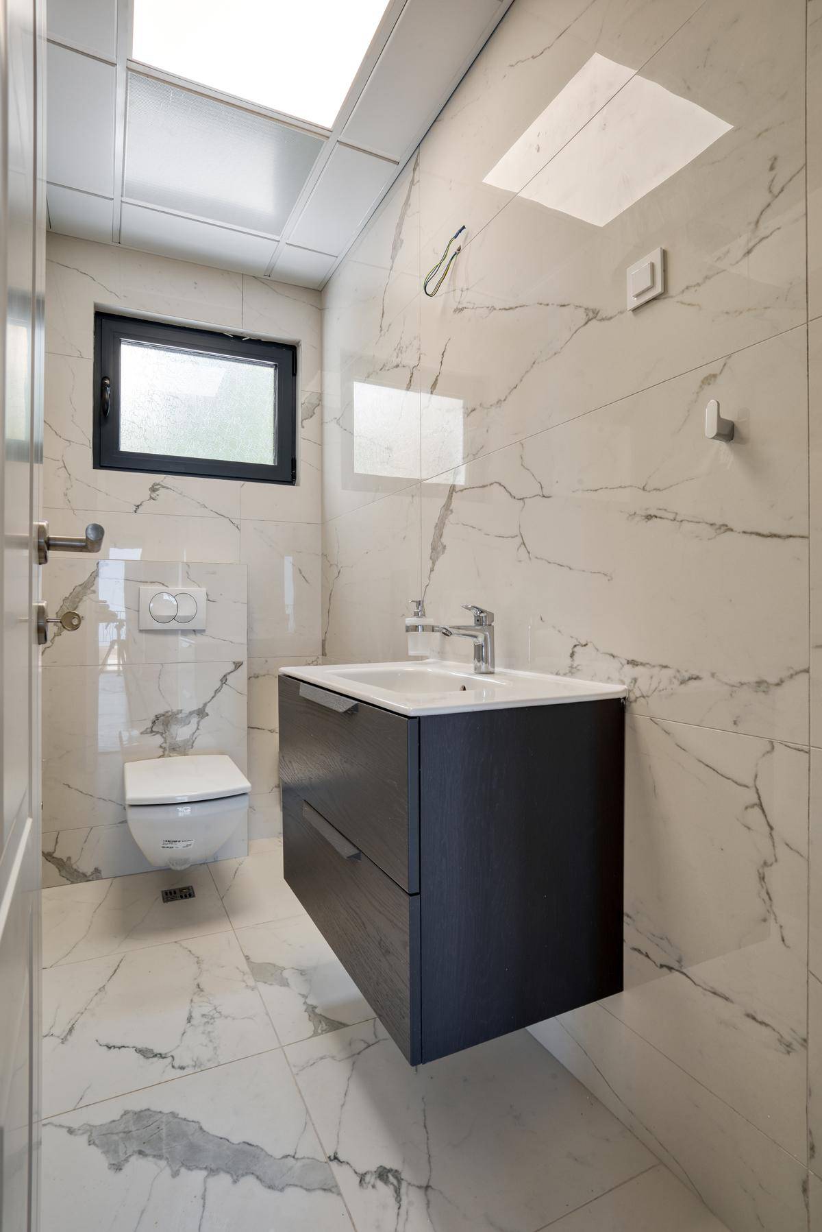 Kompaktes Gäste-WC mit modernem Waschtisch, Wand-WC und großformatigen Fliesen.