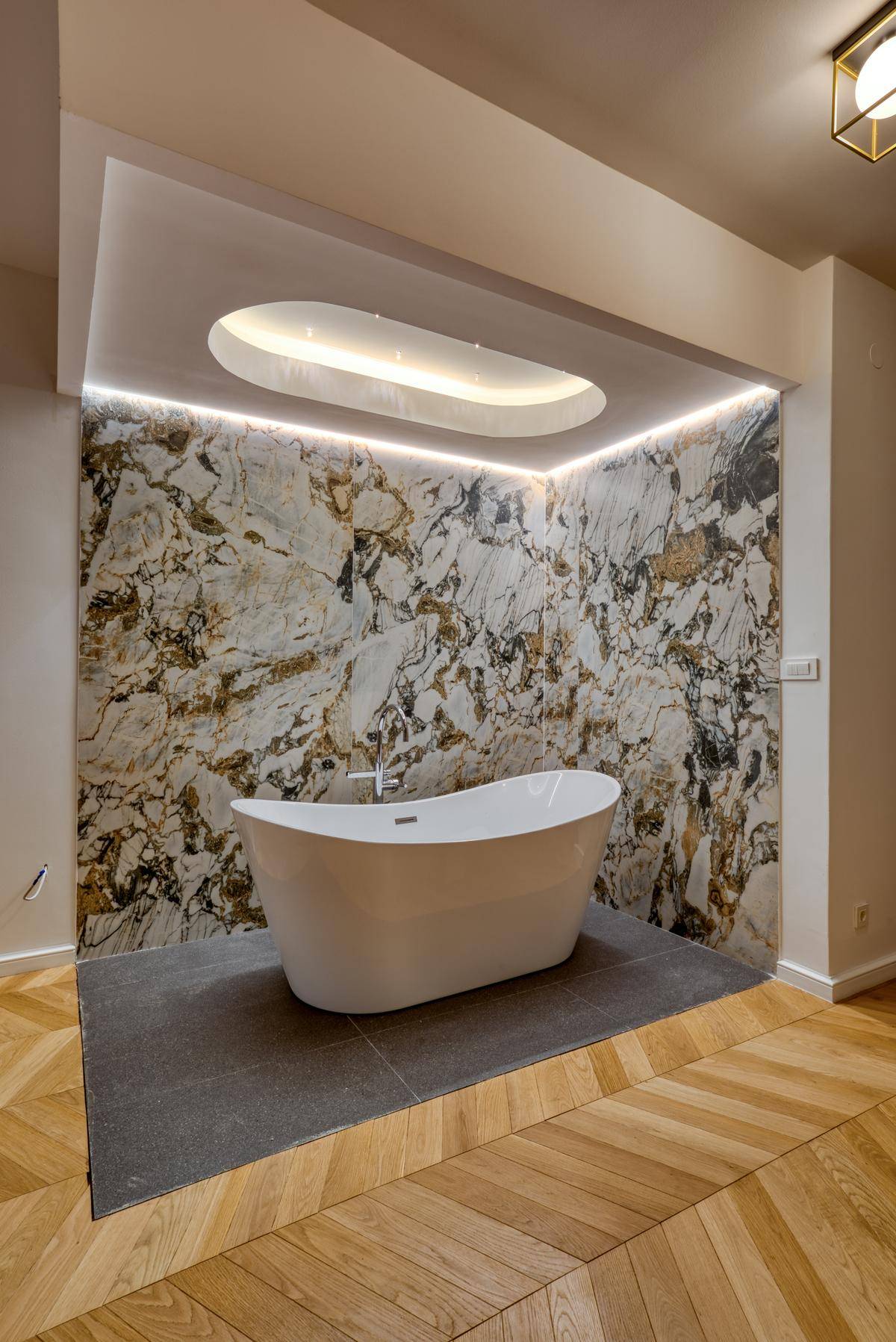 Elegante freistehende Badewanne vor einer Marmorwand in einem luxuriösen Schlafzimmerbereich.