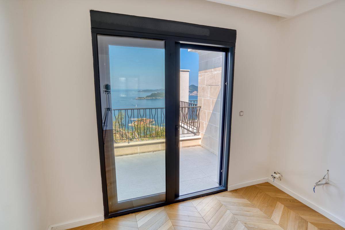 Helles Zimmer mit Fischgrätparkett und Schiebetüren, die zu einem Balkon mit weitem Meerblick führen.