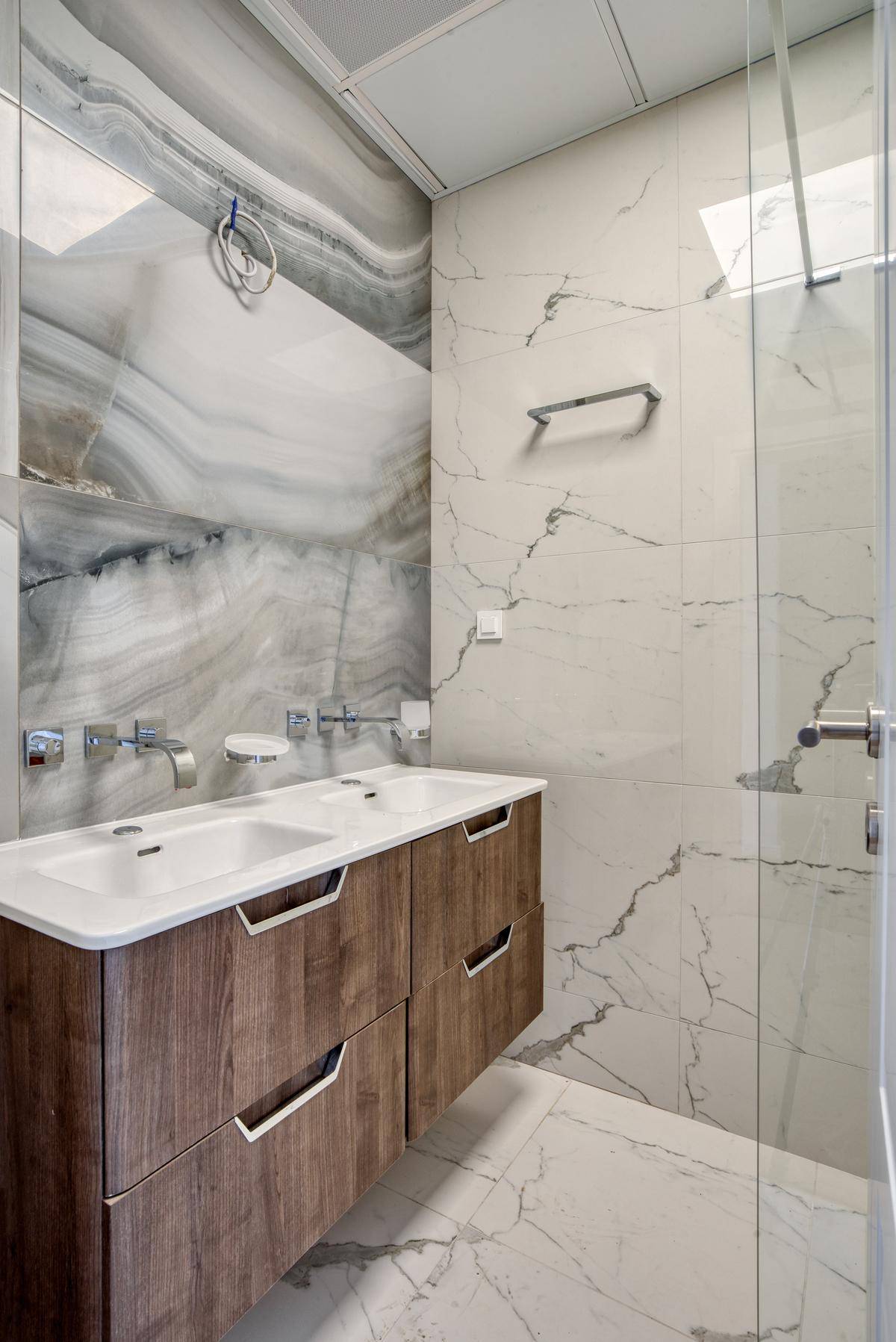 Modernes Badezimmer mit Doppelwaschbecken, schwebendem Holzunterschrank und großformatigen Marmorfliesen.