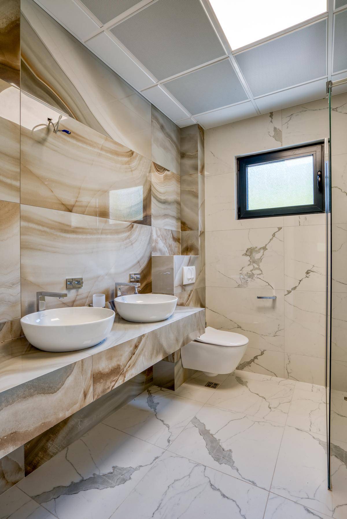 Modernes Badezimmer mit zwei Aufsatzwaschbecken, schwebendem Waschtisch und Duschbereich mit Fenster.