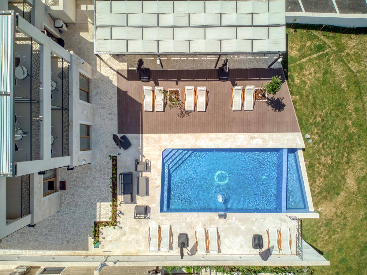 Vogelperspektive des eleganten Poolbereichs mit Holzdeck, Liegestühlen und schattigem Essbereich.