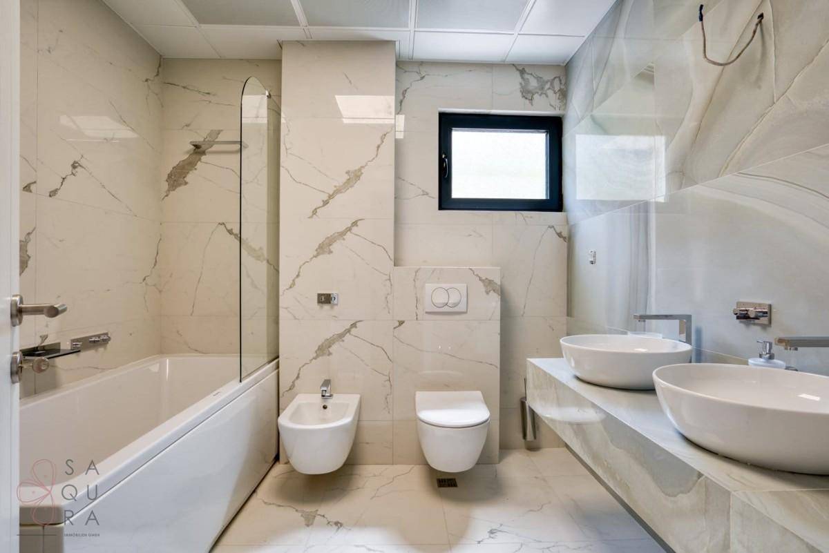 Modernes Badezimmer mit Marmorfliesen, Doppelwaschbecken, Badewanne und separatem Bidet.