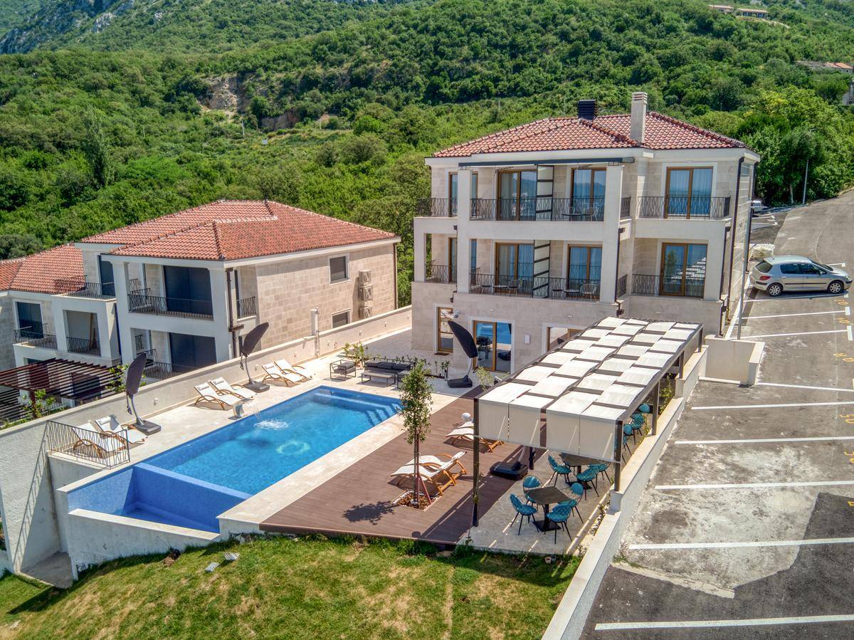 Luftaufnahme des modernen Gebäudekomplexes mit Poolbereich, Terrassen und umliegender grüner Landschaft.