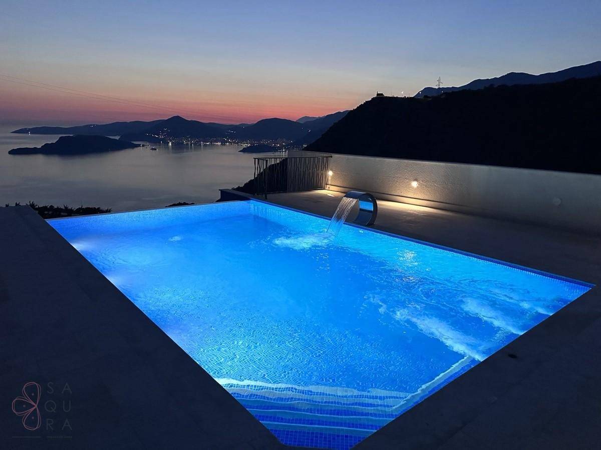 Beleuchteter Pool bei Sonnenuntergang mit Blick auf die ruhige Bucht und die umliegenden Berge.