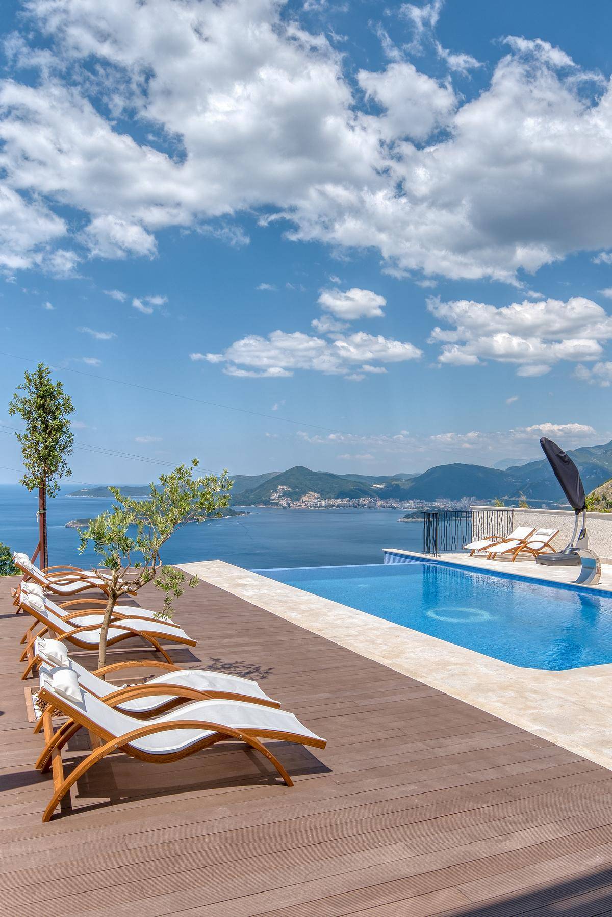 Holzterrasse mit bequemen Liegestühlen und weitem Blick über das azurblaue Meer und die Küste.