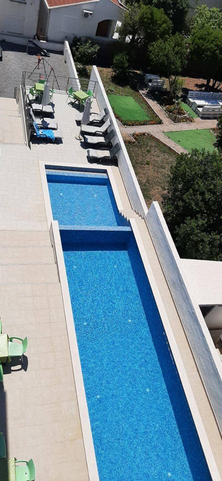 Langer, schmaler Außenpool mit blauen Fliesen und angrenzendem Liegebereich mit Sonnenliegen.