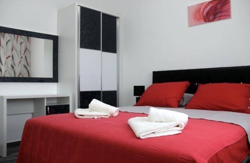 Schlafzimmer mit roter Bettwäsche, modernem Kleiderschrank und Spiegelkonsole.