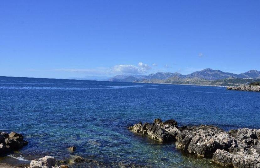 Weitläufiger Meerblick mit klarem blauen Wasser und felsiger Küste, umrahmt von fernen Bergen.