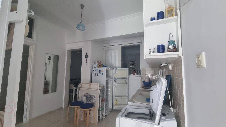 Funktionale Küche mit Kühlschrank, Waschmaschine und einfachen weißen Schränken.