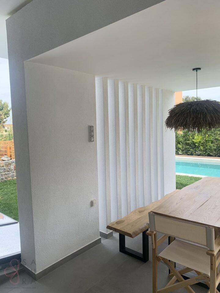 Überdachter Essbereich im Freien mit Holztisch und Blick auf den Pool und den Garten.
