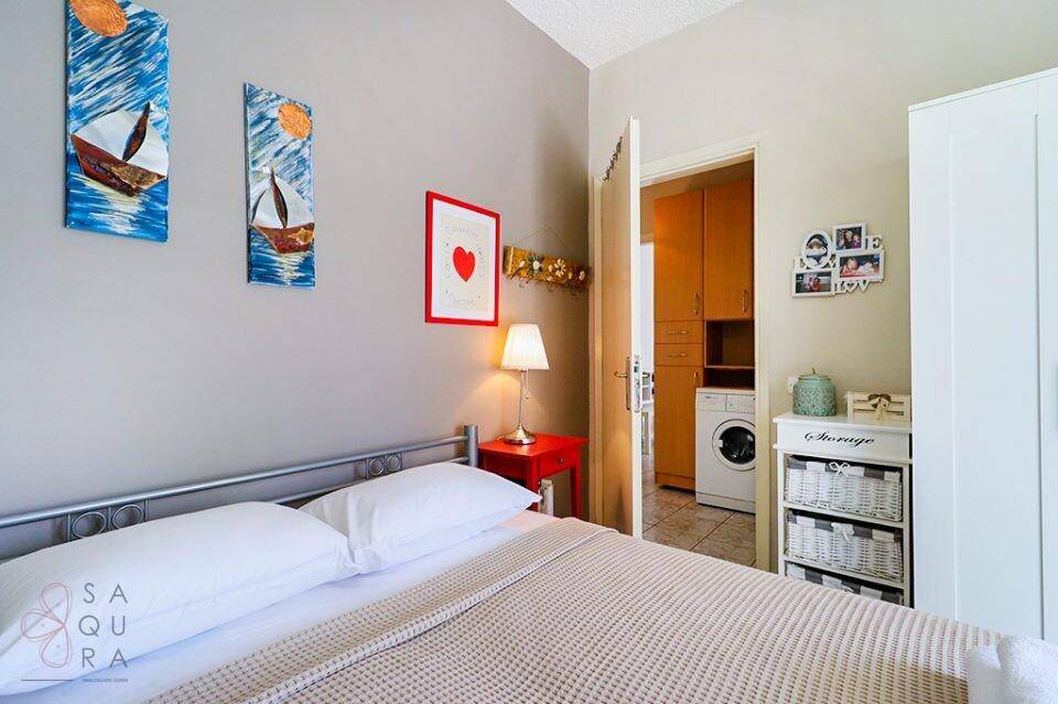 Schlafzimmer mit Doppelbett, grauer Wand und Blick in einen Hauswirtschaftsraum.