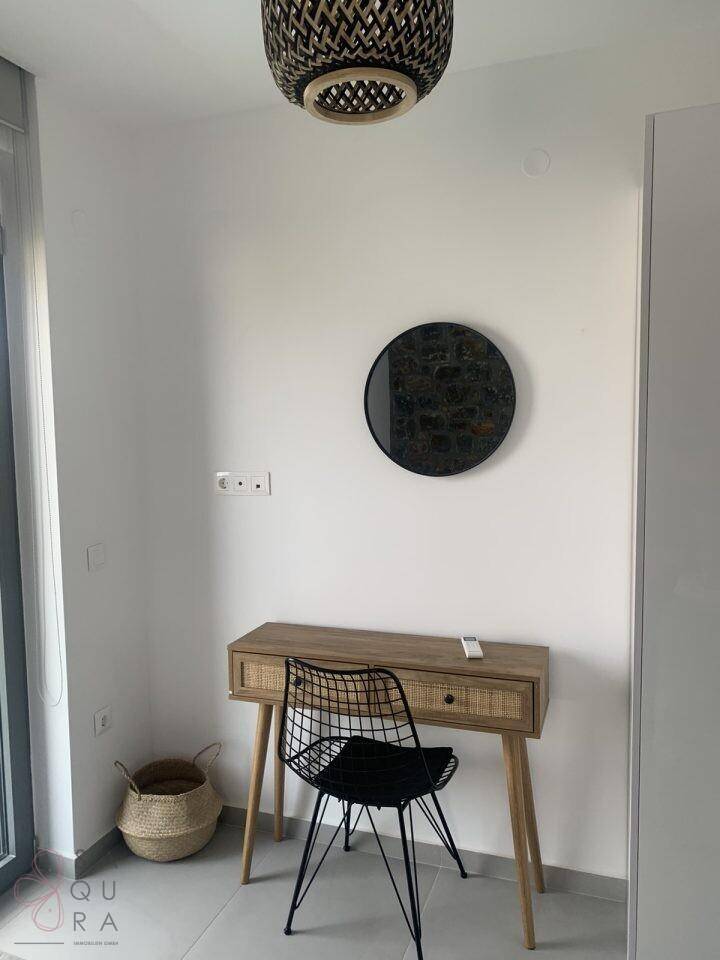 Schlafbereich mit modernem Schreibtisch, Stuhl und einem runden Spiegel an der Wand.