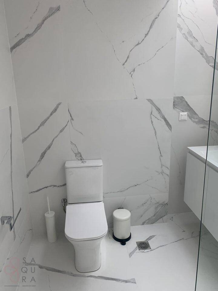 Badezimmer mit WC, Waschbecken und durchgehenden Fliesen in weißer Marmoroptik.