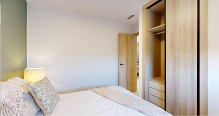 Schlafzimmer mit hellem Holzschrank und Zugang zu einem weiteren Raum, modern eingerichtet.