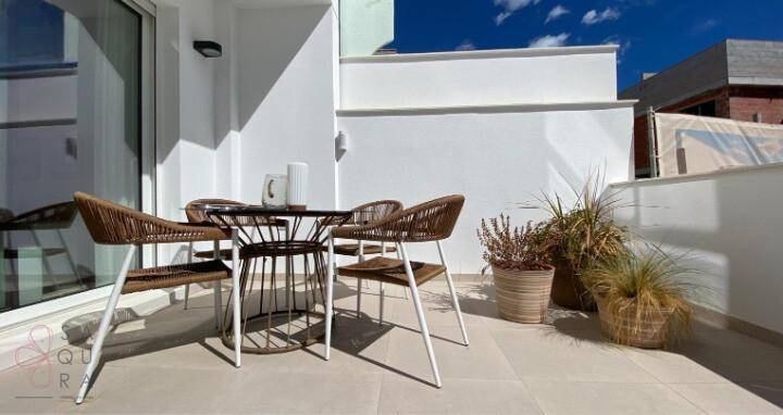 Gemütliche Terrasse mit Rattanmöbeln und Topfpflanzen unter strahlend blauem Himmel.