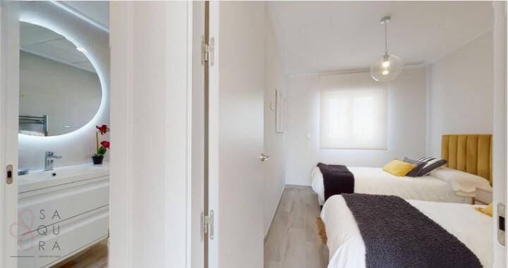 Helles Schlafzimmer mit zwei Einzelbetten und Zugang zu einem modernen Badezimmer.