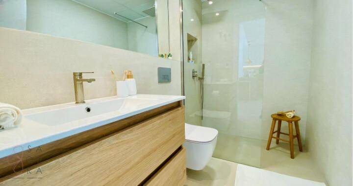 Helles Badezimmer mit Einzelwaschbecken, wandhängender Toilette und begehbarer Dusche.