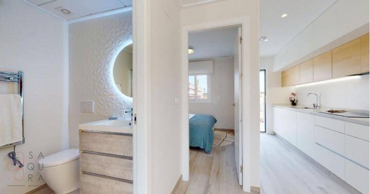 Modernes Badezimmer mit beleuchtetem Spiegel, Einzelwaschbecken und Blick in die Küche und Schlafzimmer.