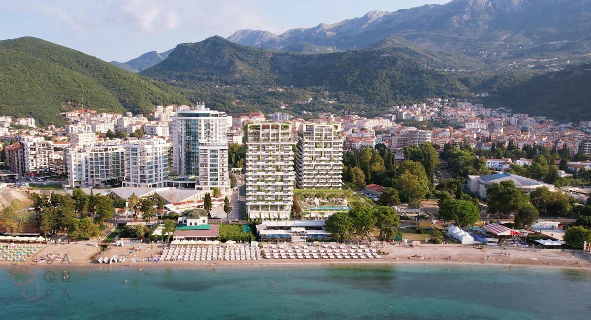 Luftaufnahme des modernen Gebäudekomplexes am Strand mit Bergen im Hintergrund.