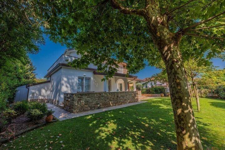 Seitlicher Blick auf das Haus mit Steinmauer, gepflastertem Weg und üppiger grüner Bepflanzung.