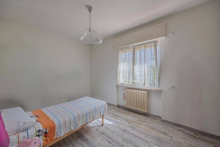 Helles Schlafzimmer mit Einzelbett, Heizkörper und einem Fenster mit Vorhängen.