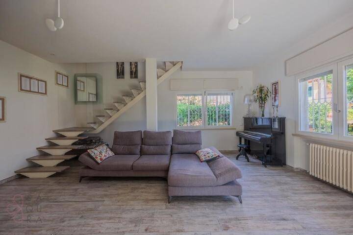 Geräumiges Wohnzimmer mit bequemer Couch, offener Treppe und einem eleganten Klavier.