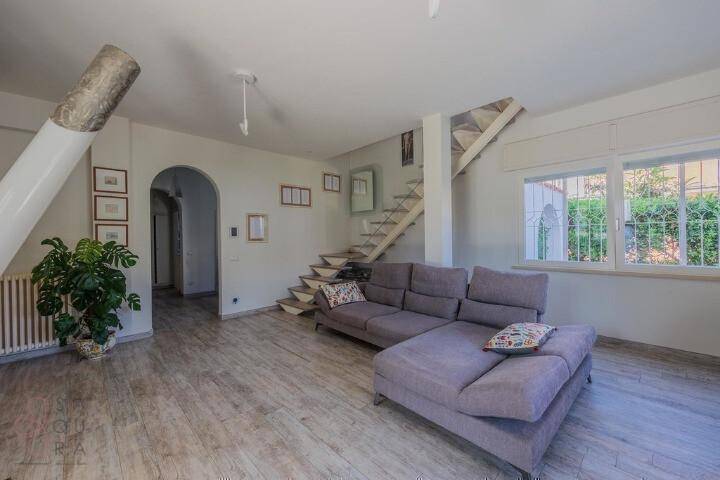 Helles Wohnzimmer mit großem Ecksofa, offener Treppe und Blick in den Flur.