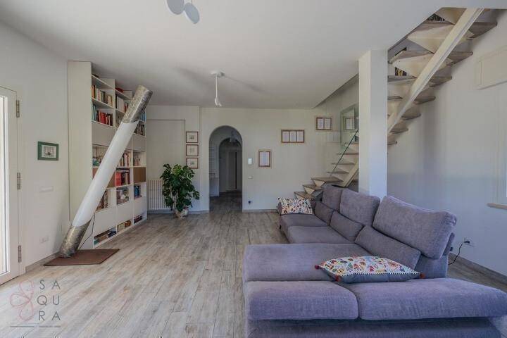 Wohnzimmer mit gemütlichem Sofa, offener Treppe und einem großen Bücherregal als Blickfang.
