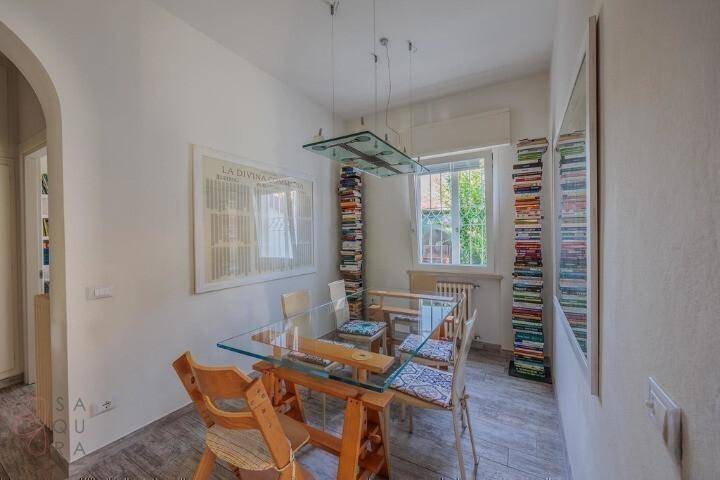 Helles Esszimmer mit Glastisch, Holzstühlen und kreativen Bücherstapeln als Dekoration.