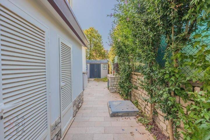 Seitlicher gepflasterter Weg entlang des Hauses mit einem kleinen Schuppen im Hintergrund.