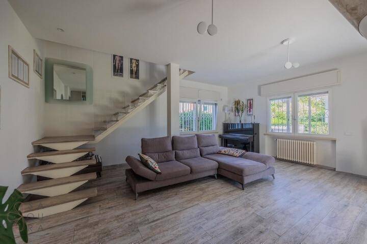 Helles Wohnzimmer mit bequemer Couch, offener Treppe und einem stilvollen Klavier.