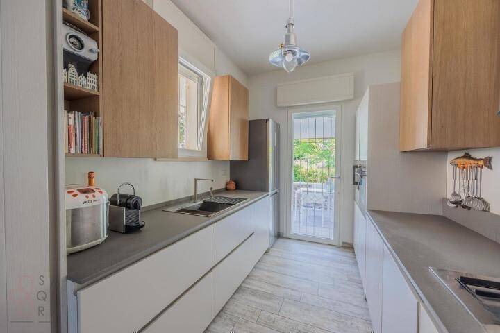 Funktionale moderne Küche mit weißen und holzfarbenen Schränken, Spüle und Kaffeemaschine.