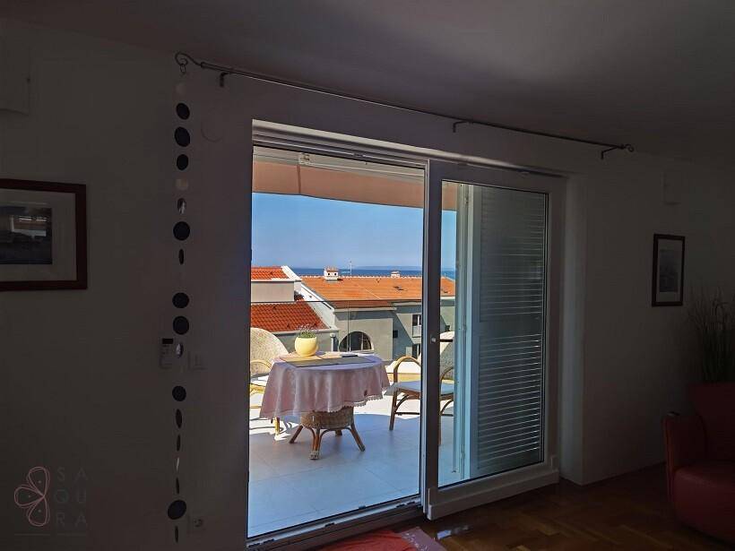 Wohnzimmer mit großen Schiebetüren, die den Blick auf den möblierten Balkon und das Meer freigeben.