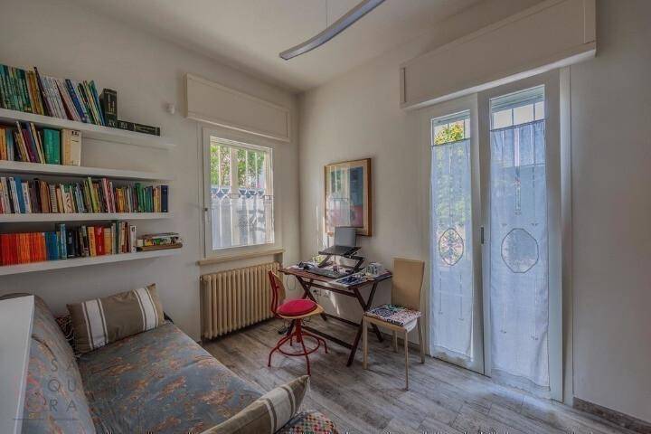 Helles Zimmer mit Tagesbett, Bücherregalen und einem Arbeitsbereich am Fenster.
