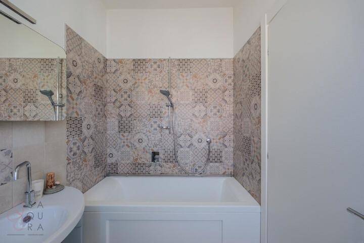 Badezimmer mit Badewanne und Duschfunktion, umgeben von dekorativen Fliesen.