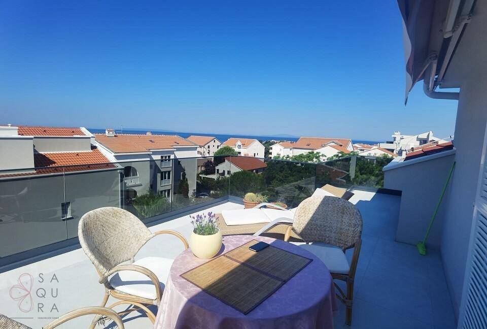 Heller Balkon mit Sitzgelegenheiten und weitem Blick über die Dächer zum Meer.