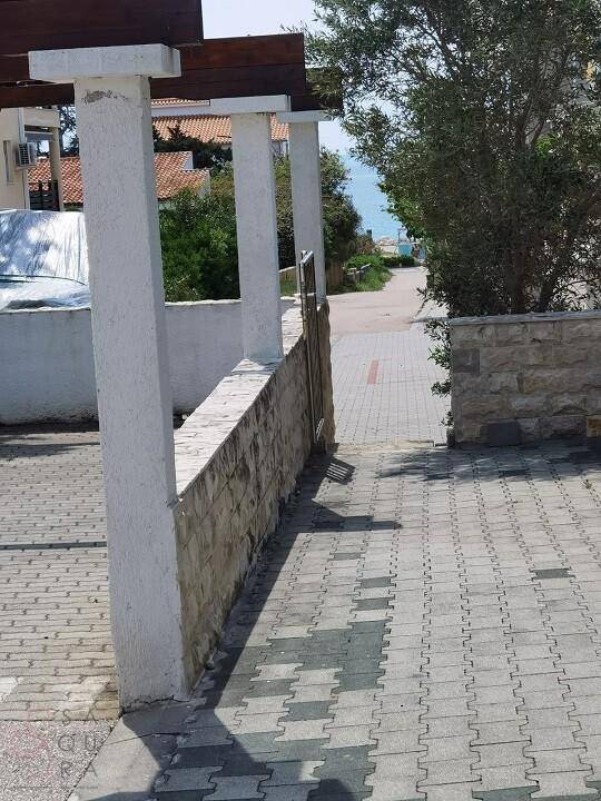Gepflasterter Außenbereich mit Steinmauer und Säulen, der zum Meer führt.