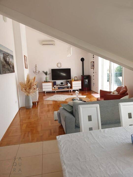 Gemütliches Wohnzimmer mit Dachschräge, Parkettboden, Fernseher und einem modernen Holzofen.
