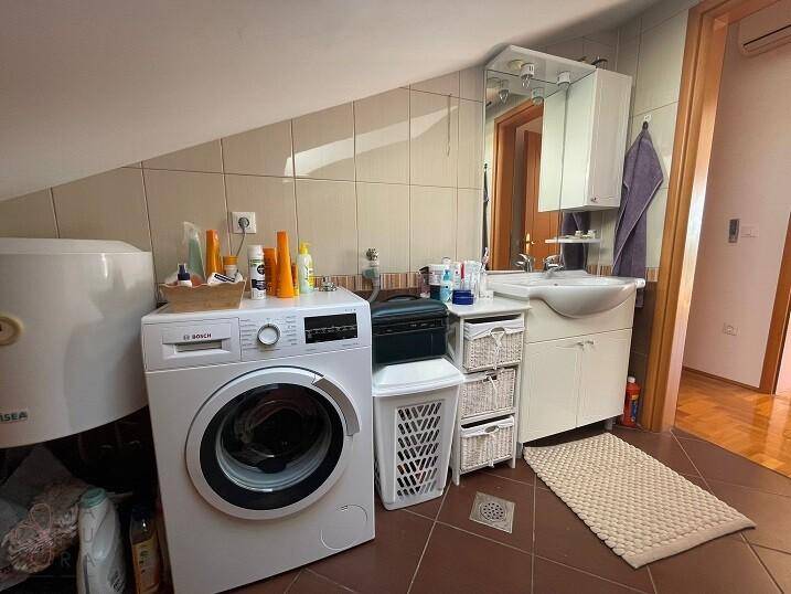 Funktionales Badezimmer mit Fliesen, Waschbecken, Spiegelschrank und Waschmaschine.