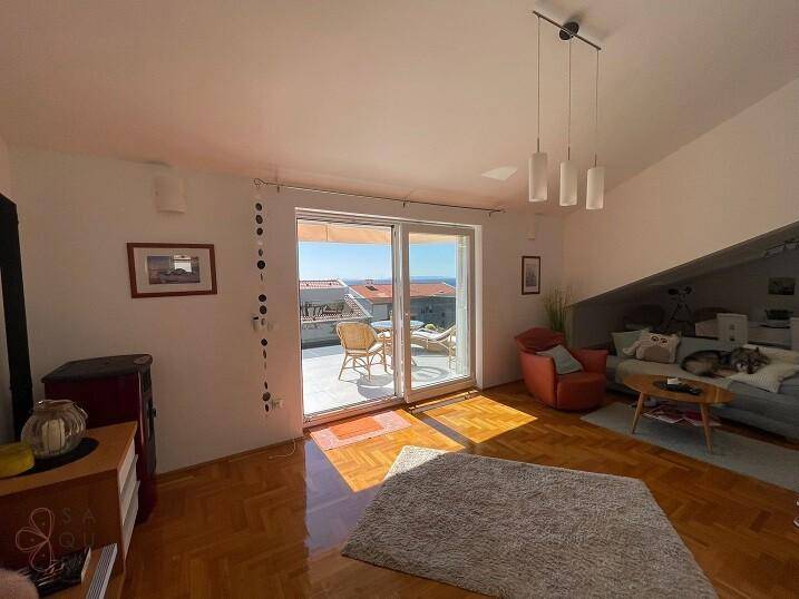 Geräumiges Wohnzimmer mit Dachschräge, Parkettboden und hellem Zugang zum Balkon mit Meerblick.