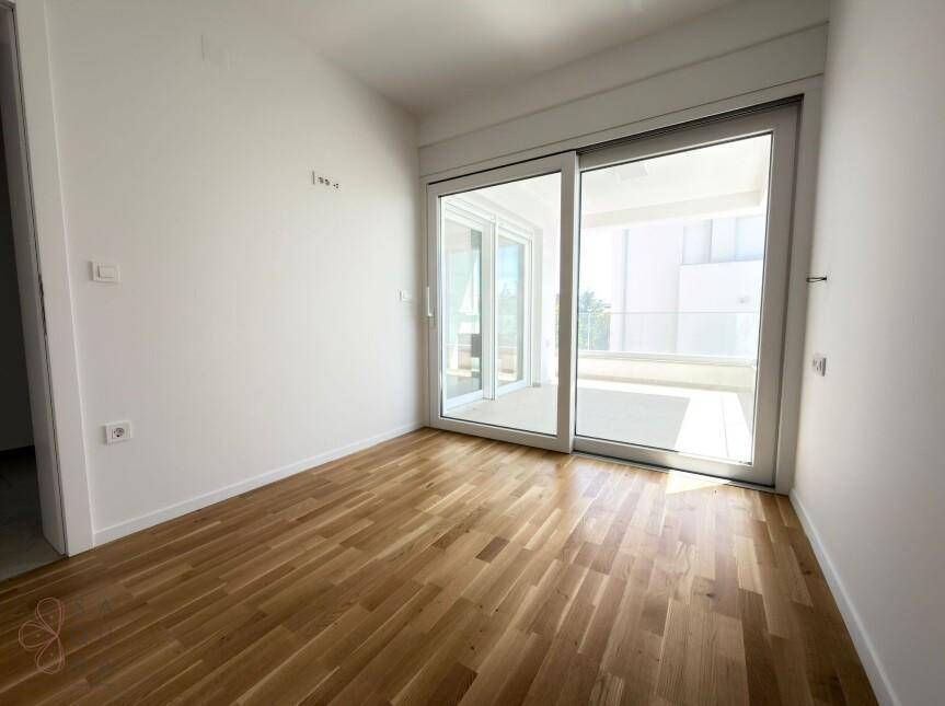 Lichtdurchfluteter Raum mit Holzboden und großen Schiebetüren zum Balkon.
