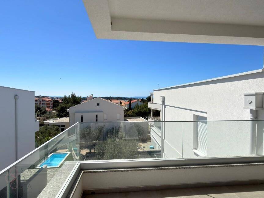Geräumiger Balkon mit Glasgeländer und weitem Blick über die Nachbarschaft bis zum Meer.