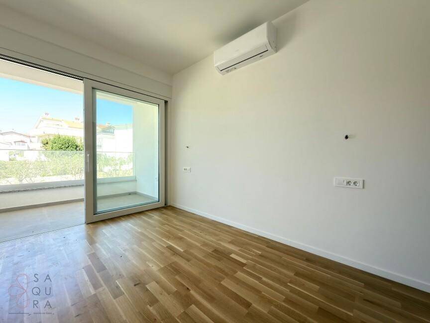 Lichtdurchfluteter Raum mit Holzboden, Klimaanlage und Schiebetür zum Balkon.