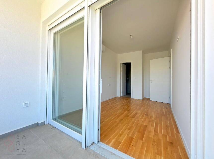Heller Raum mit Holzboden und Zugang zu einem sonnigen Balkon.